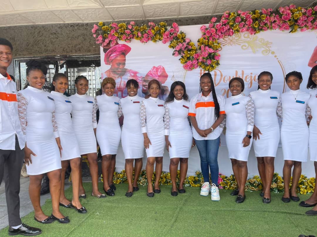 A twelve-strong usher team in white in front of a rose-dressed birthday backdrop