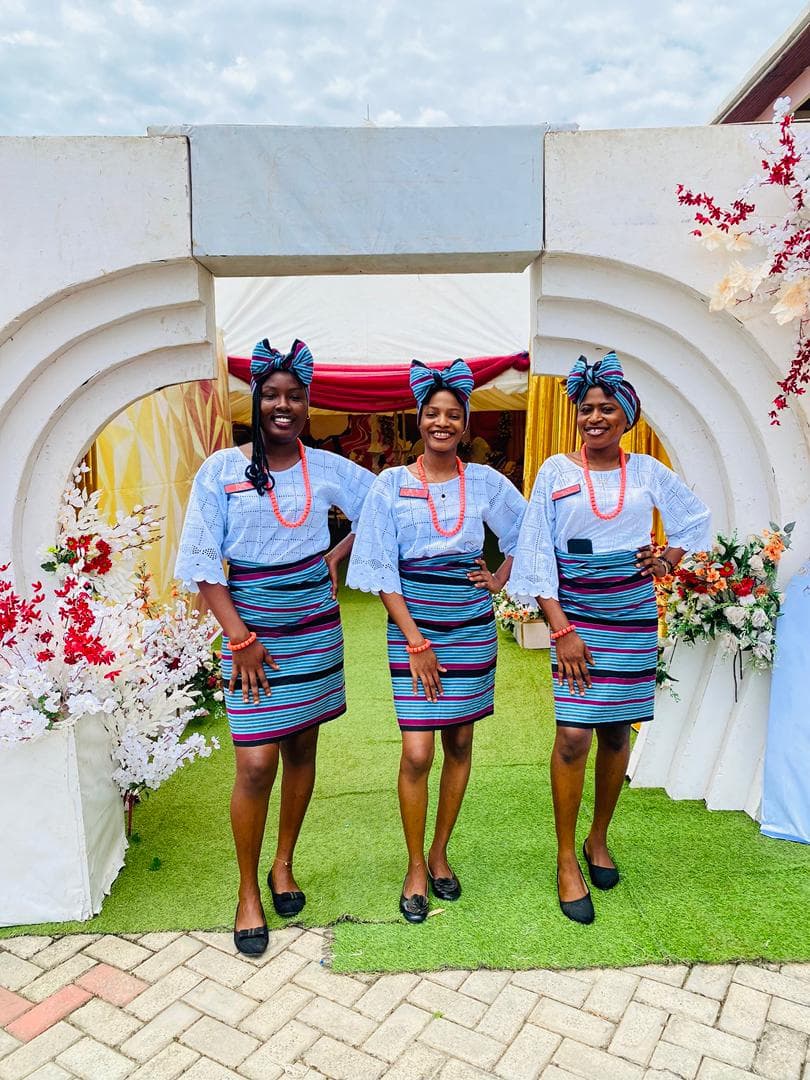 Three ushers welcoming guests at a white arched entrance banked with red and white florals
