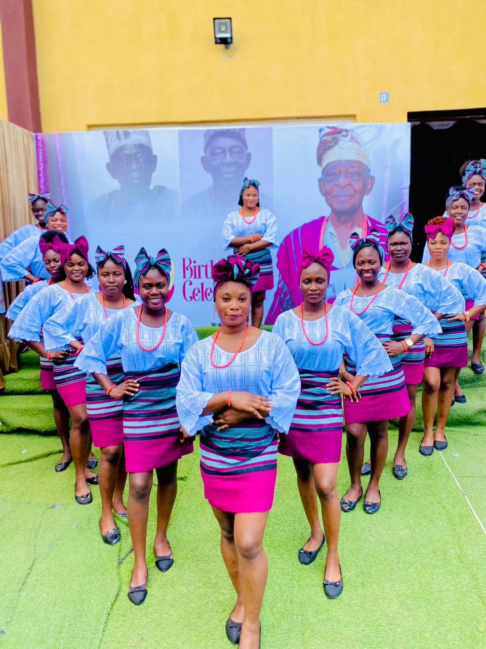 Ushers in blue and magenta uniforms in formation in front of a birthday celebration banner